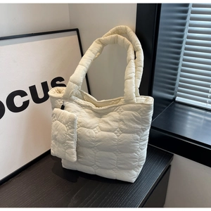 Détail du sac cabas matelassé blanc avec sa mini pochette sur une surface en bois