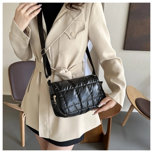 Close-up of black quilted pillow bag with glossy finish and adjustable strap worn on coat