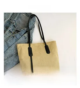 Detail of beige corduroy tote bag featuring black leather straps on denim background
