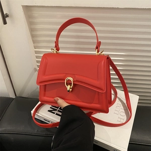 Elegant red structured handbag with gold oval clasp on a black leather tabletop