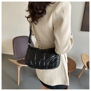 Detail of black quilted puffy shoulder bag with gold hardware on a beige coat