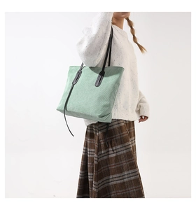 Detail of light green corduroy tote bag with black handles on a model in studio light