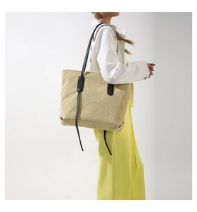 Detail of a large beige woven tote bag with slim black leather straps on a model