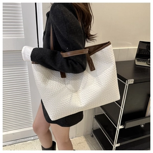 Détail d'un cabas blanc à texture tressée et anses marron porté par un mannequin