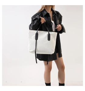 Close-up of the textured white corduroy fabric and black leather handles on a tote bag