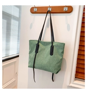 Detail of sage green corduroy tote bag with black straps hanging on a wooden hook