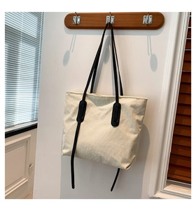 Detail of off-white corduroy tote bag with black leather reinforcement on a wooden hook