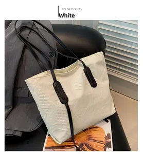 Detail of white corduroy tote bag showing ribbed texture and black leather strap on a chair