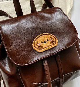 Detail shot of brown faux leather backpack featuring cute dog plush embroidery and flap