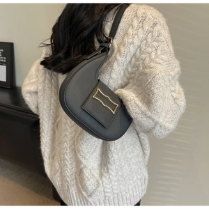 Detail of black crescent shoulder bag with gold geometric buckle on white knit sweater