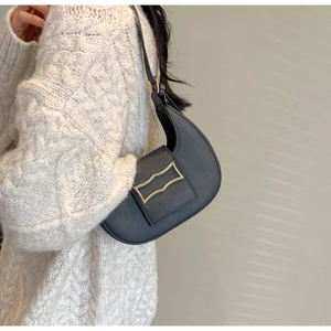 Detail of a black half-moon shoulder bag with golden buckle on a white knit sweater
