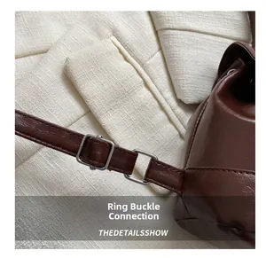 Detail view of the metal buckle connection on a brown leather backpack strap