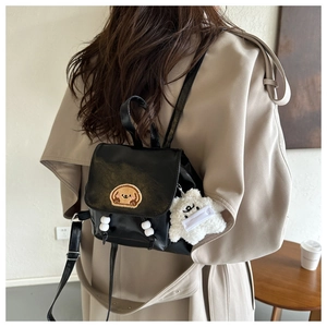 Detail view of black leather backpack with cartoon dog embroidery and plush bear charm