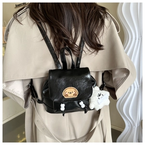 Detail of black PU leather mini backpack with puppy embroidery and plush charm decoration