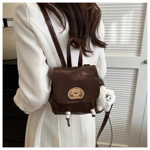 Mini brown leather backpack with cartoon bear patch and plush charm on a model