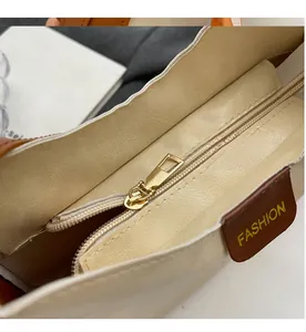 Detail of a smooth golden metal zipper on a soft beige faux leather tote bag with tag