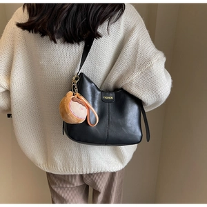 Detail of minimalist black soft leather tote with FASHION logo and plush charm