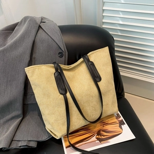 Minimalist beige corduroy tote bag with black faux leather handles on a chic leather chair