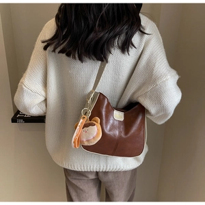 Detail of dark brown leather tote bag with plush bear charm and contrast shoulder strap