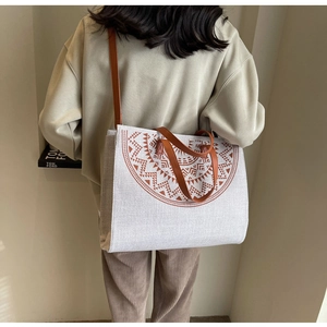 Close-up of a large beige linen tote bag featuring a brown tribal totem and leather handles