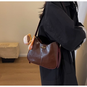 Detail of dark brown leather tote bag featuring fashion metal logo and burger plush charm