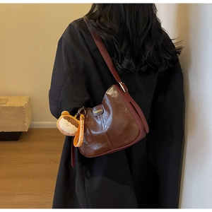 Brown leather tote bag featuring a cute bear keychain shown on a female model's shoulder