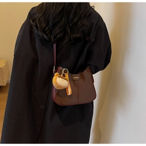 Detail of dark brown faux leather shoulder bag with plush charm on a model