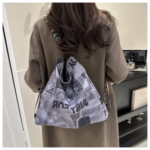 Detail van krantenprint draagtas met LOVE-band gedragen op een stijlvolle trenchcoat