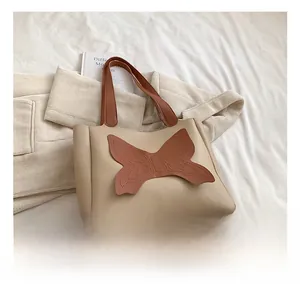Close-up of beige faux leather tote bag featuring a decorative brown butterfly patch