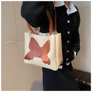 Close-up of matte cream faux leather tote bag with large brown butterfly patch and stitching