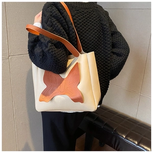 Shoulder shot of a beige leather tote bag featuring a large brown butterfly patch detail