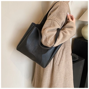 Detail of a large black leather tote bag featuring elegant butterfly stitching and shoulder strap