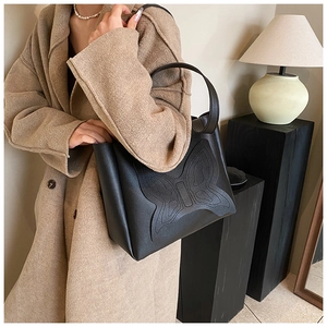 Detail of black leather tote bag featuring a 3D butterfly embossed pattern and wide handles