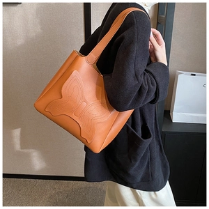 Close-up of caramel brown tote bag featuring detailed butterfly stitching and leather texture