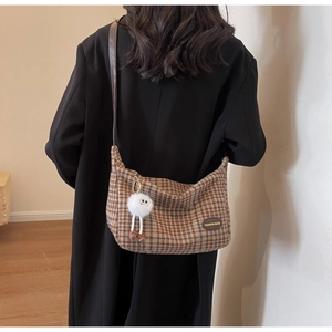 Detailed view of brown plaid shoulder bag with soft fuzzy doll pendant and leather tag