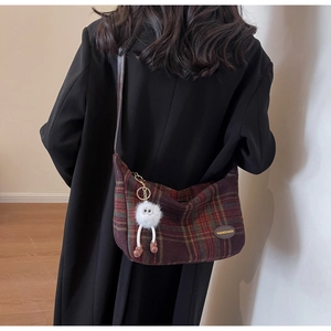 Detail of red plaid wool shoulder bag with plush pendant on black coat