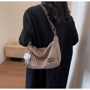 Close-up of retro plaid crescent bag with brown leather strap and plush ball charm