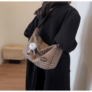 Detail of vintage brown plaid shoulder bag with leather strap and plush monster charm