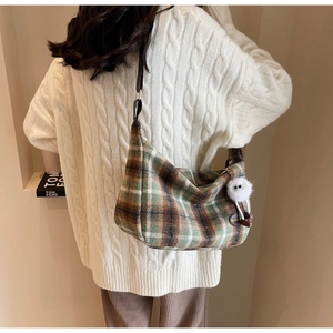 Detailed view of a green plaid shoulder bag with a white fluffy eyeball charm on a model