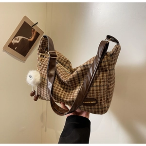 Close-up of retro plaid shoulder bag with leather strap and plush ball charm accessory