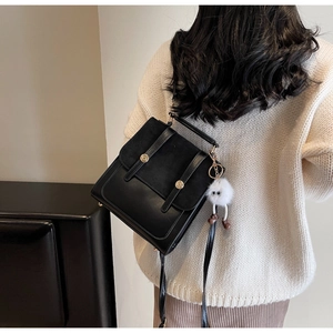 Detail of black mixed-material backpack with gold hardware and plush charm on white sweater