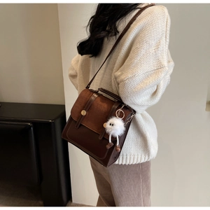 Detail of vintage brown messenger bag with plush charm on a model's knit sweater