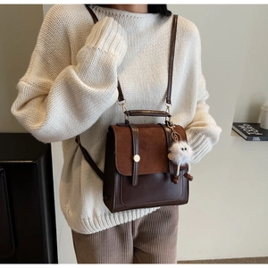 Close-up of a dual-texture brown backpack with a plush doll charm and gold ring clasp