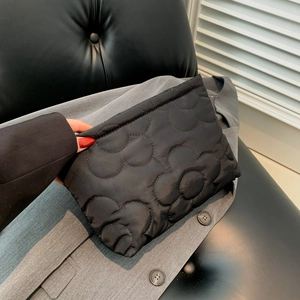 Modieuze zwarte gewatteerde clutch met bloemenpatroon vastgehouden bij grijs pak