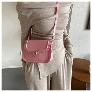 Détail du sac bandoulière rose avec boucle dorée et texture cuir porté par un mannequin
