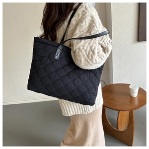 Detail view of a large black quilted tote bag with diamond stitching shown on a model