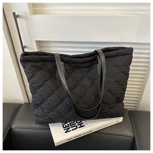 Detailed view of black quilted tote bag with diamond stitching and leather handles