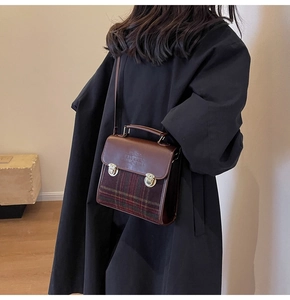 Detail of vintage brown leather satchel with plaid fabric and gold metal buckles