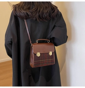 Brown leather and red tartan plaid crossbody bag shown on a model in a black coat