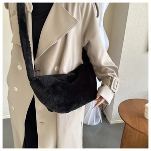 Close-up of fluffy black plush dumpling bag with wide shoulder strap on a beige coat